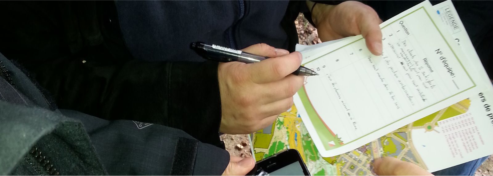 Une équipe en pleine nature, résolvant une énigme de l'orient'SCORE trouvée
      à l'aide d'une carte de course d'orientation.