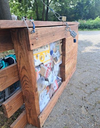 Coffre en bois avec vitre transparente. IL est fermé par un cadenas et contient des déchets.