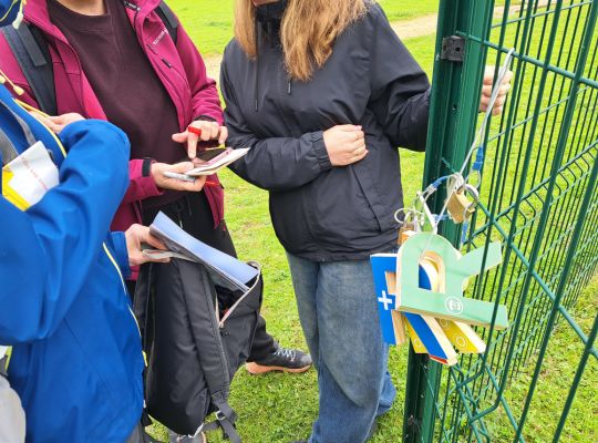 Des participants autour d'une énigme complètement nomade et fixée sur une clôture en extérieur.